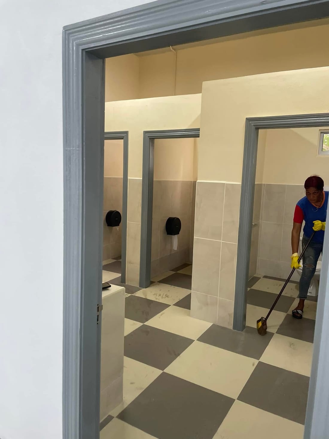 A CDCS worker cleaning the tiled floor of a commercial restroom
